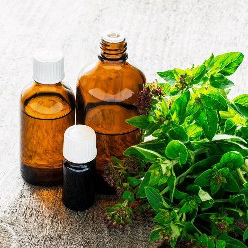 Three amber bottles with essential oils next to fresh green herbs, perfect for creating unique fragrance blends.