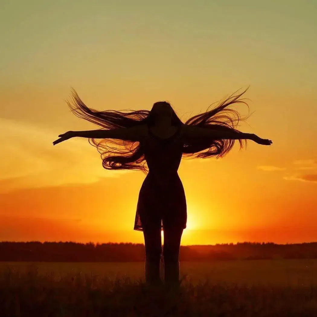 Silhouette of a woman with outstretched arms at sunset, embodying freedom and elegance.