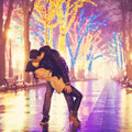 Couple sharing a romantic kiss under colorful lights in a beautifully lit park.