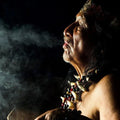 Elder exhaling smoke in a mystical ambiance, adorned with tribal jewelry, embodying spiritual essence.