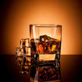 Glass of amber whiskey on the rocks with ice cubes against a warm orange backdrop.