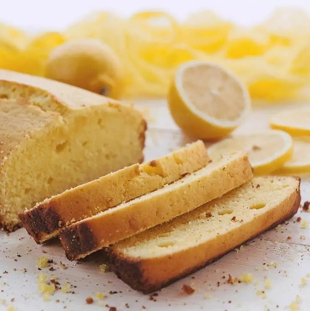 Freshly sliced lemon pound cake with lemons in the background, showcasing a delightful blend of citrus scents.