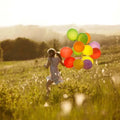 A girl runs joyfully in a field, holding a colorful bouquet of balloons against a sunny backdrop.