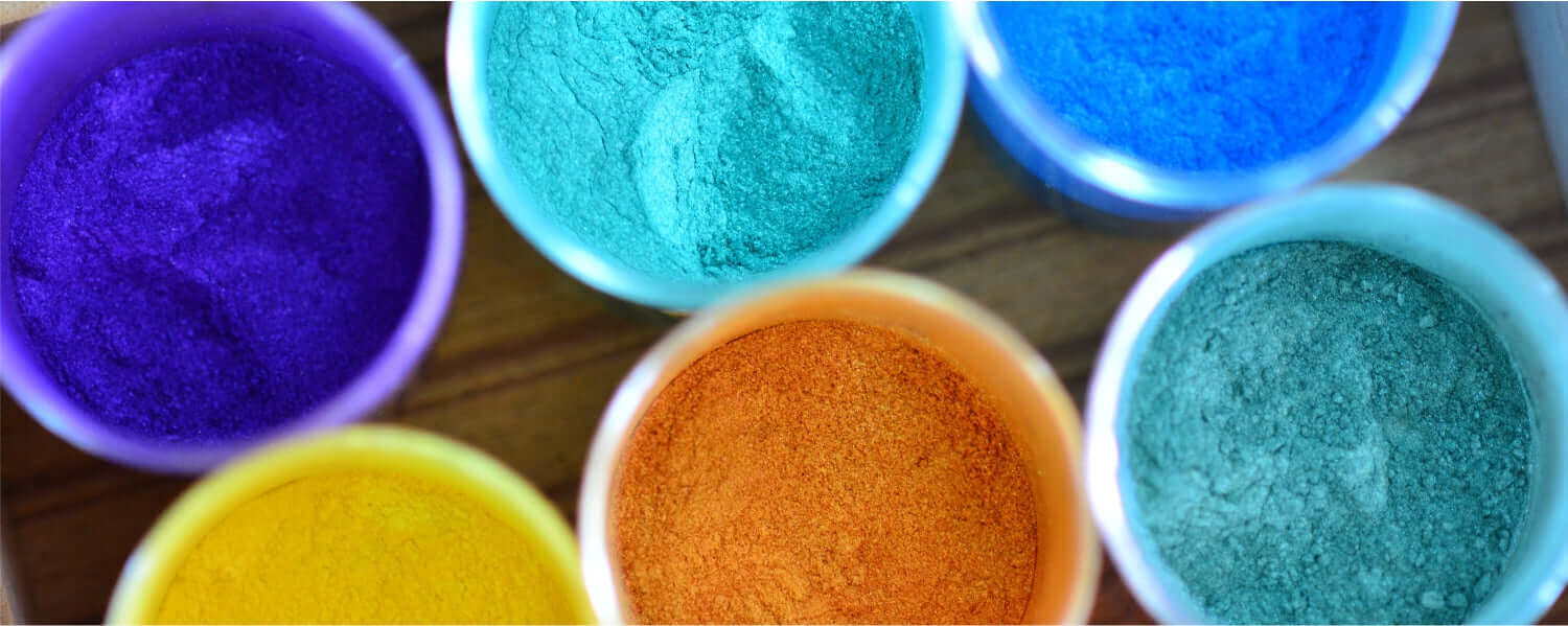 Vibrant colored powders in cups, showcasing a bright palette of purple, blue, green, orange, and yellow hues.