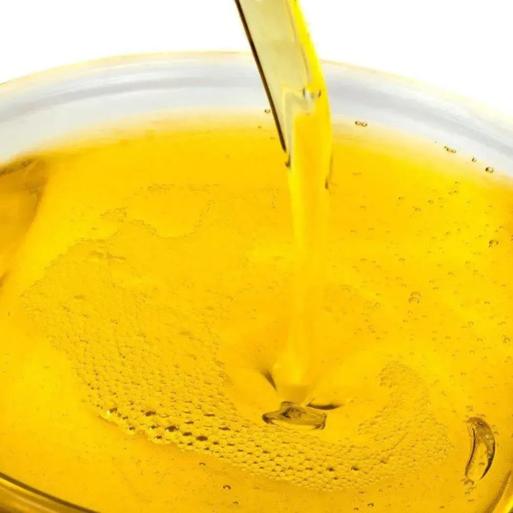 Pouring a rich golden oil blend for soap making, showcasing its smooth texture and quality.