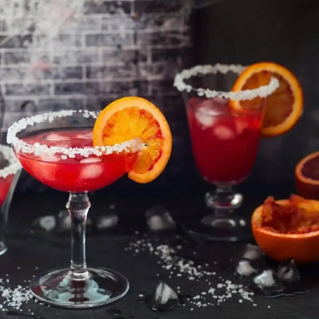 Vibrant orange cocktails with a salted rim and ice, garnished with fresh orange slices on a dark background.