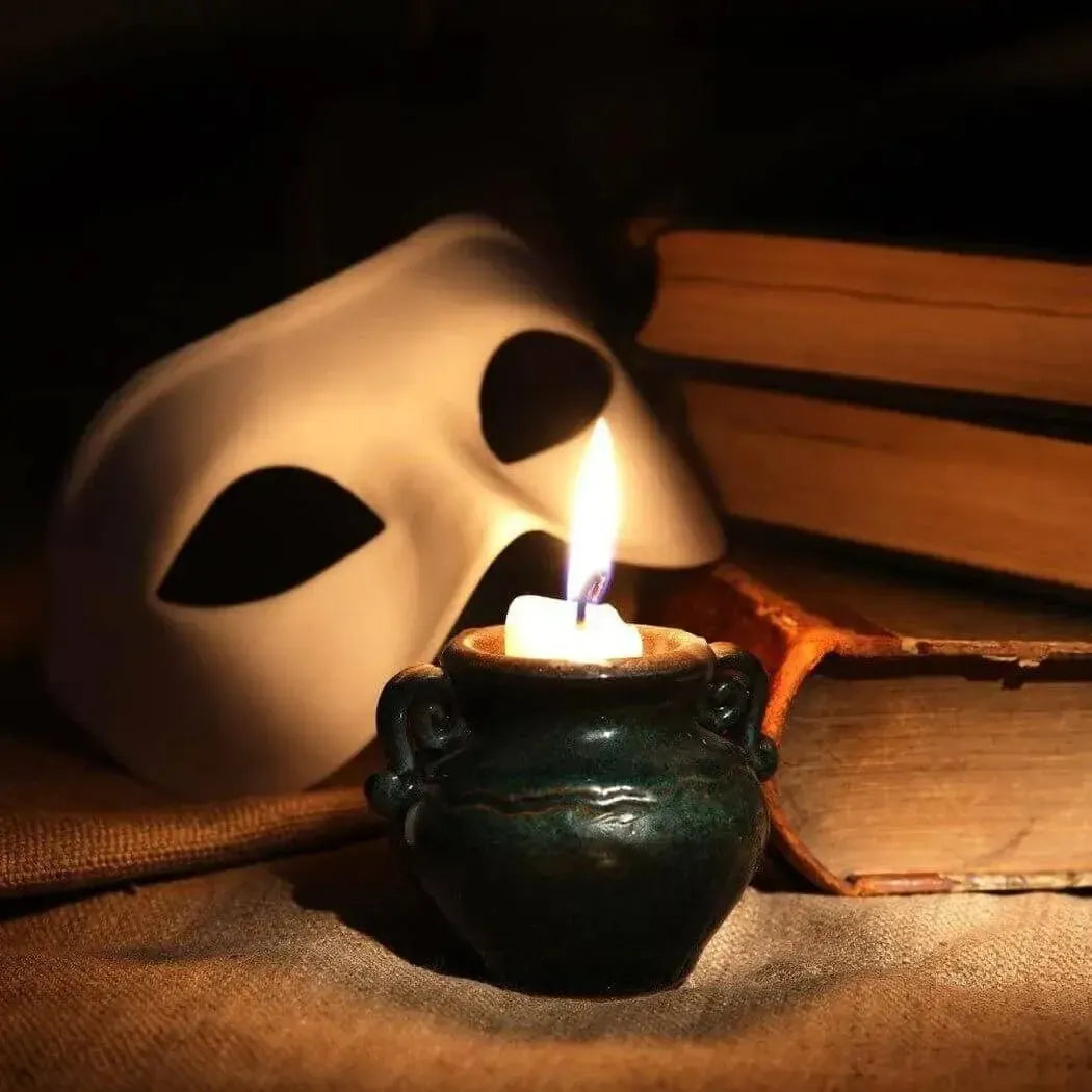 A glowing candle beside a dark mask and stacked books, creating an enchanting and mysterious ambiance.