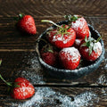 Bowl of fresh strawberries dusted with powdered sugar on a rustic wooden table, ready to sweeten any creation.